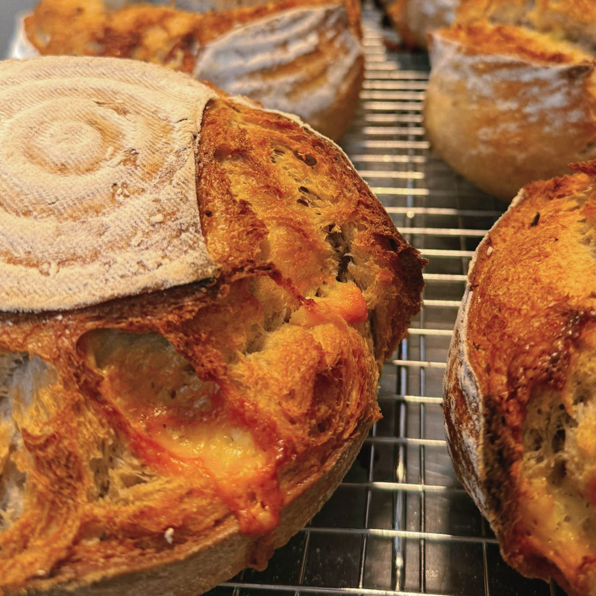 Freshly baked sourdough bread loaves cooling on a metal wire rack, with a close-up view of the golden-brown crust and flour-dusted tops.